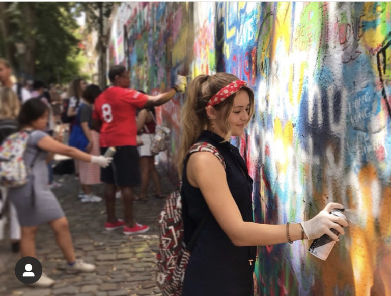 this photo shows Bella Almeida spraypainting the Earthy Creations logo on a wall in Prague