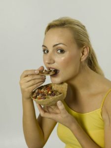 this photo shows a young woman eating food from an edible bowl