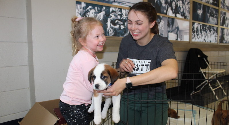 this photo shows Neely Griggs, 2020 recipient of the Algernon Sydney Sullivan Award and an animal welfare advocate, handing a puppy to a little girl at Mississippi Mutts in Oxford, Mississippi.