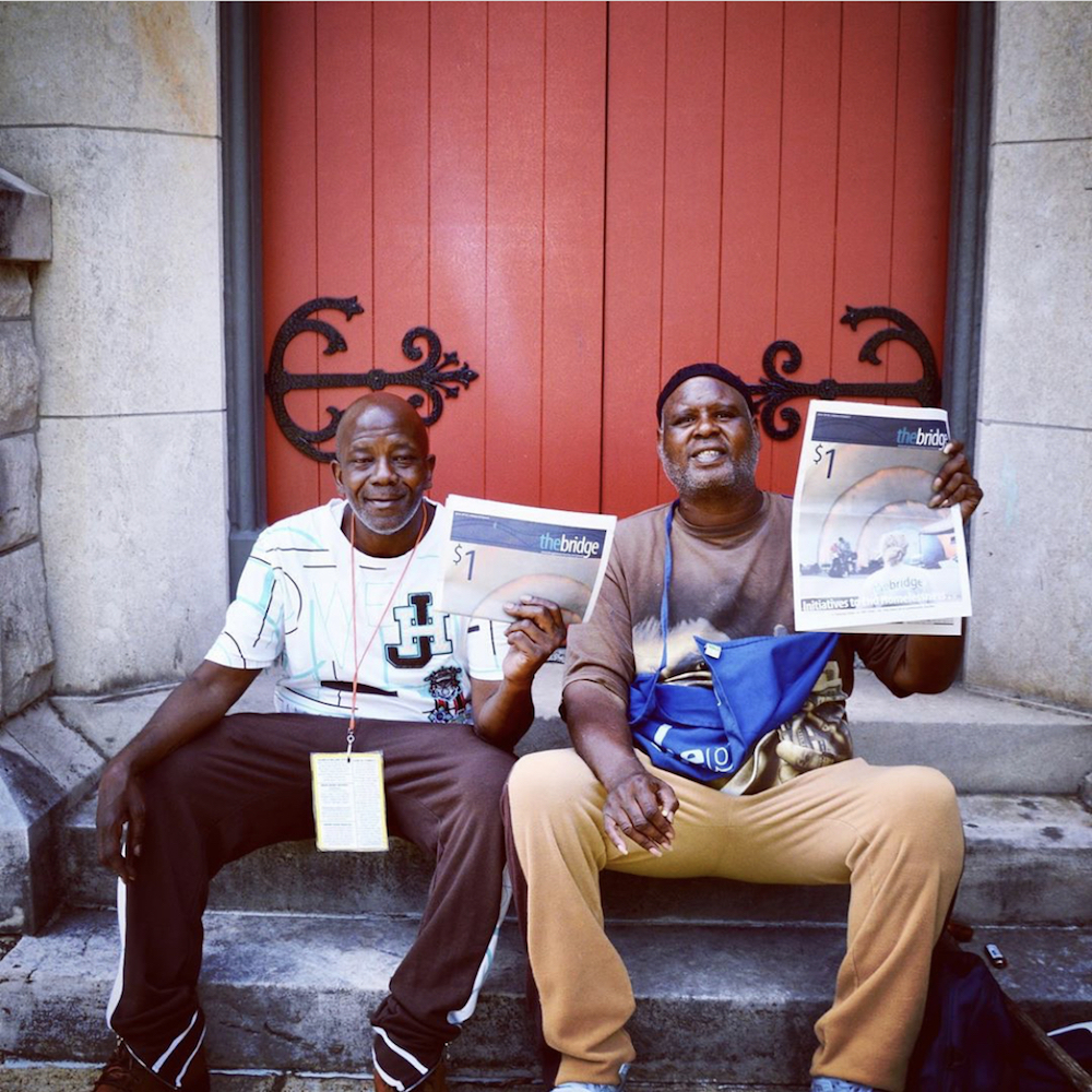 this photo depicts two men holding up a copy of the Memphis street newspaper, The Bridge