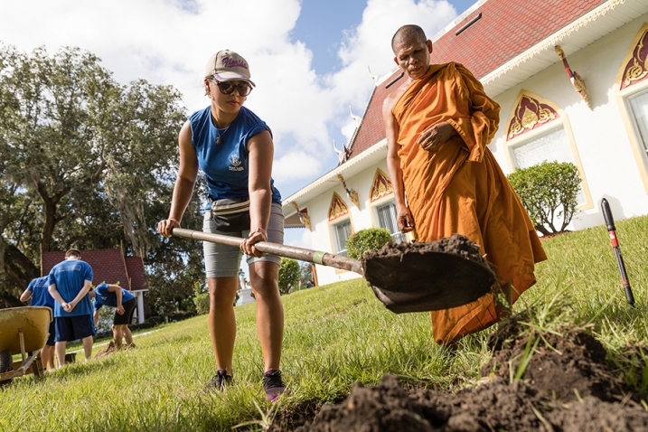 a Rollins College student digs a hole at a Buddhist temple while a monk watches on during a SPARC Day community service event