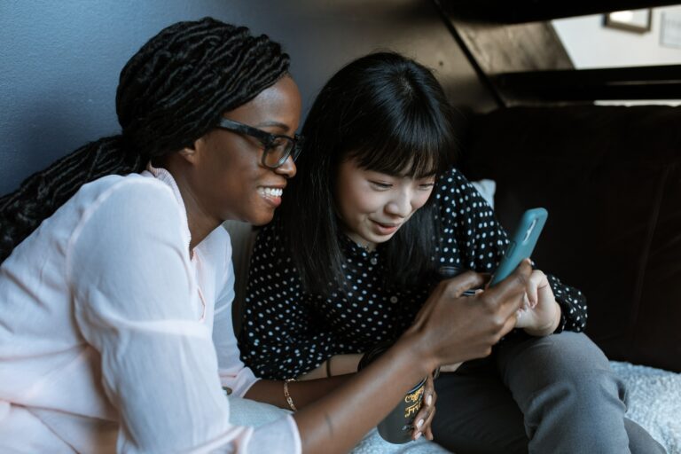 Two women in their 30s looking at a phone together and smiling.